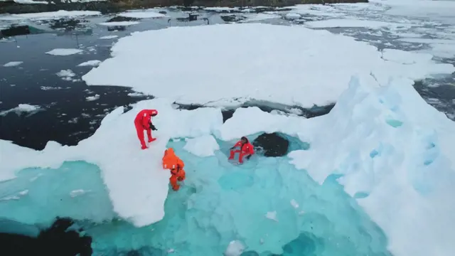 Science exploration on South Pole. People explore global warming in Antarctica. Group of scientists in orange wetsuits take samples and measure melting glacier water, climate change problem. Aerial