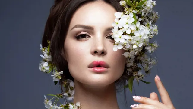 Beautiful brunette girl in blue dress with a gentle romantic make-up, pink lips and flowers. The beauty of the face. Portrait shot in the studio.