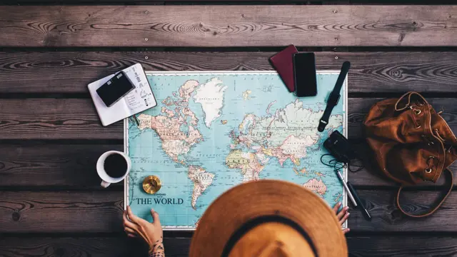 Young woman planning vacation using world map and compass along with other travel accessories. Tourist wearing brown hat looking at the world map.